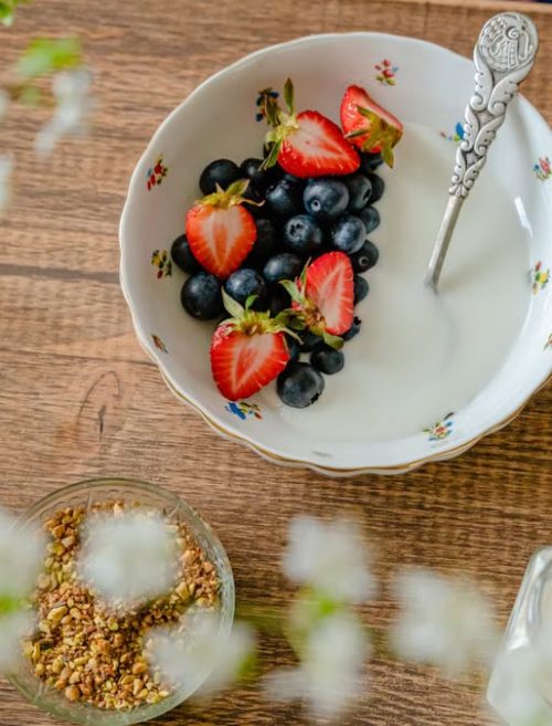 A bowl of fresh strawberries, blueberries with yogurt on a wooden table, viewed from above.
